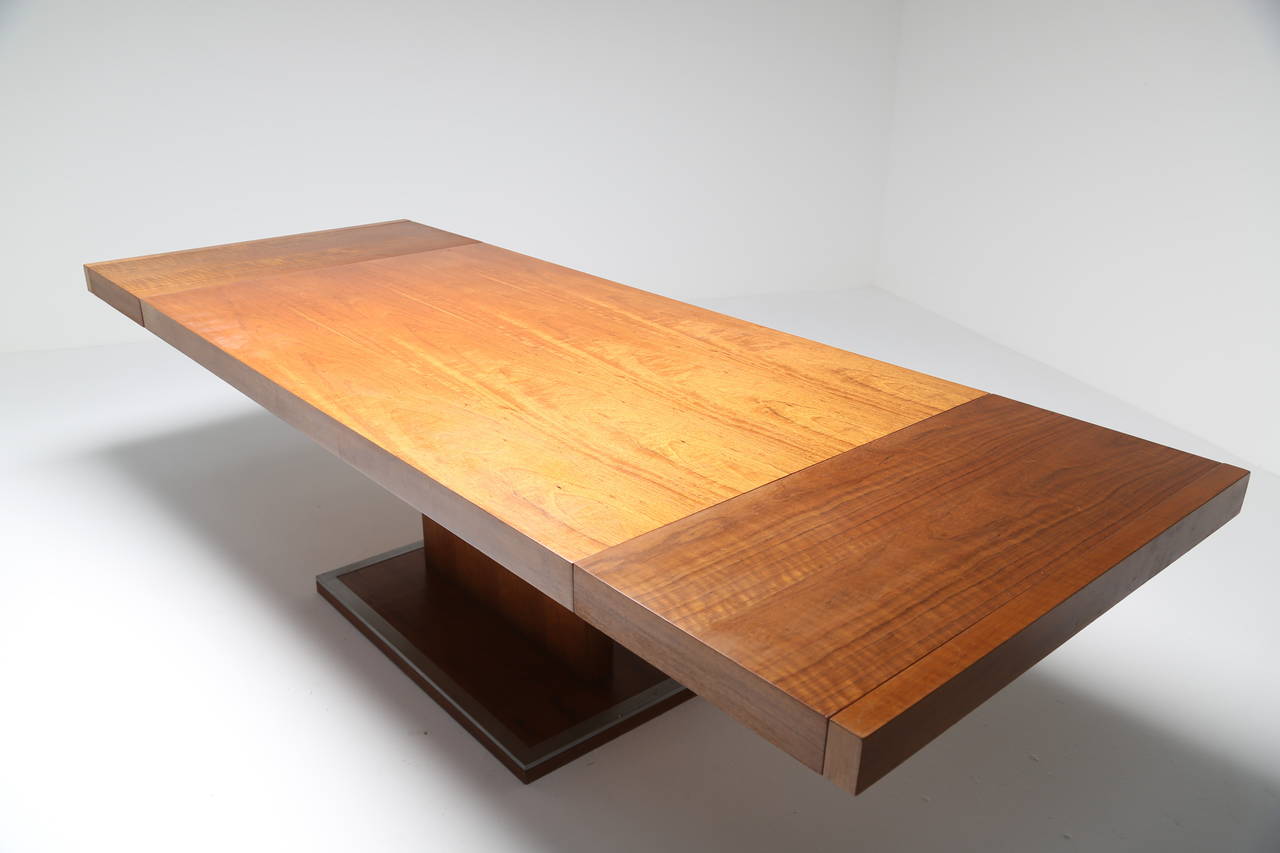 A gorgeous walnut dining table, made in the USA by Founders. The table has two removable extension leaves. The table sits beautifully on a thin vertical beam and the base of the table has a brushed steel trim. This is a real beauty of a table when