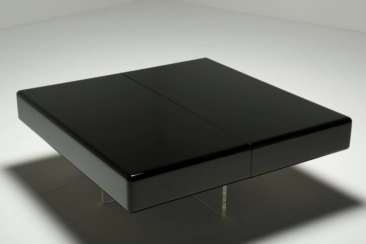 A Black lacquered coffee table that opens in the centre to reveal hidden storage below. The table sits on crossed perspex /Lucite legs. Both top pieces slide to open a storage compartment. Everything works perfectly and the table has been resprayed