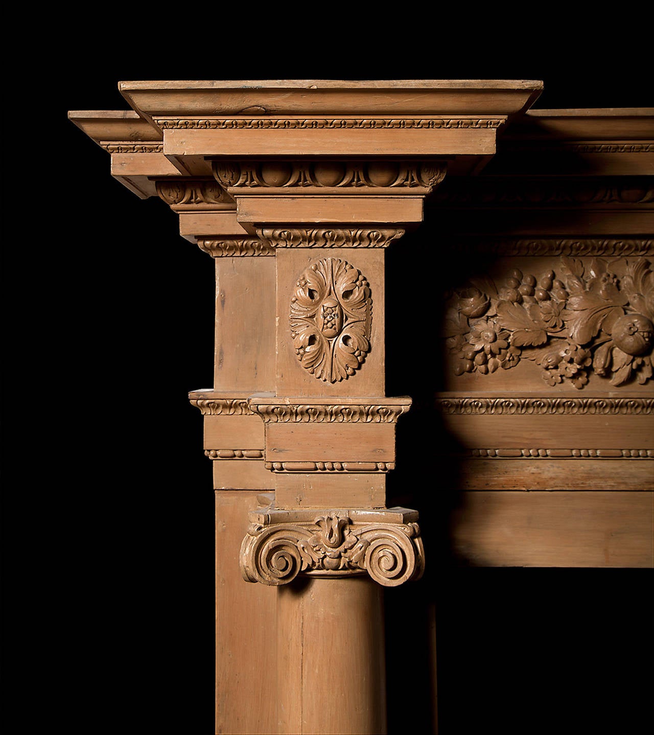 A carved pine fireplace in the Georgian manner having intricately carved panels of foliage and fruits below a carved egg and dart break front cornice. The ionic columns are full free standing which support a finely carved bead and reel architrave