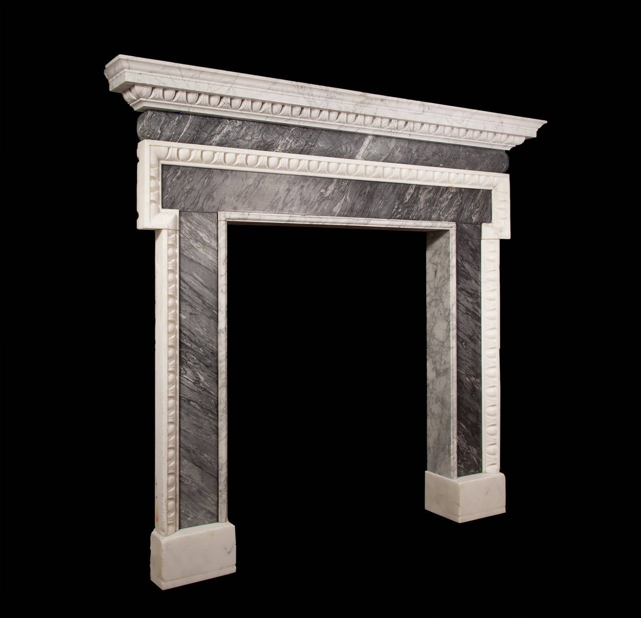 The grey Bardiglio marble frieze is barrel shaped and decorated with garlands of oak leaves and acorns, tied by ribbon in the centre. This is upheld by dogleg jambs carved with egg and bellflower mouldings. The Carrara marble shelf with pencil
