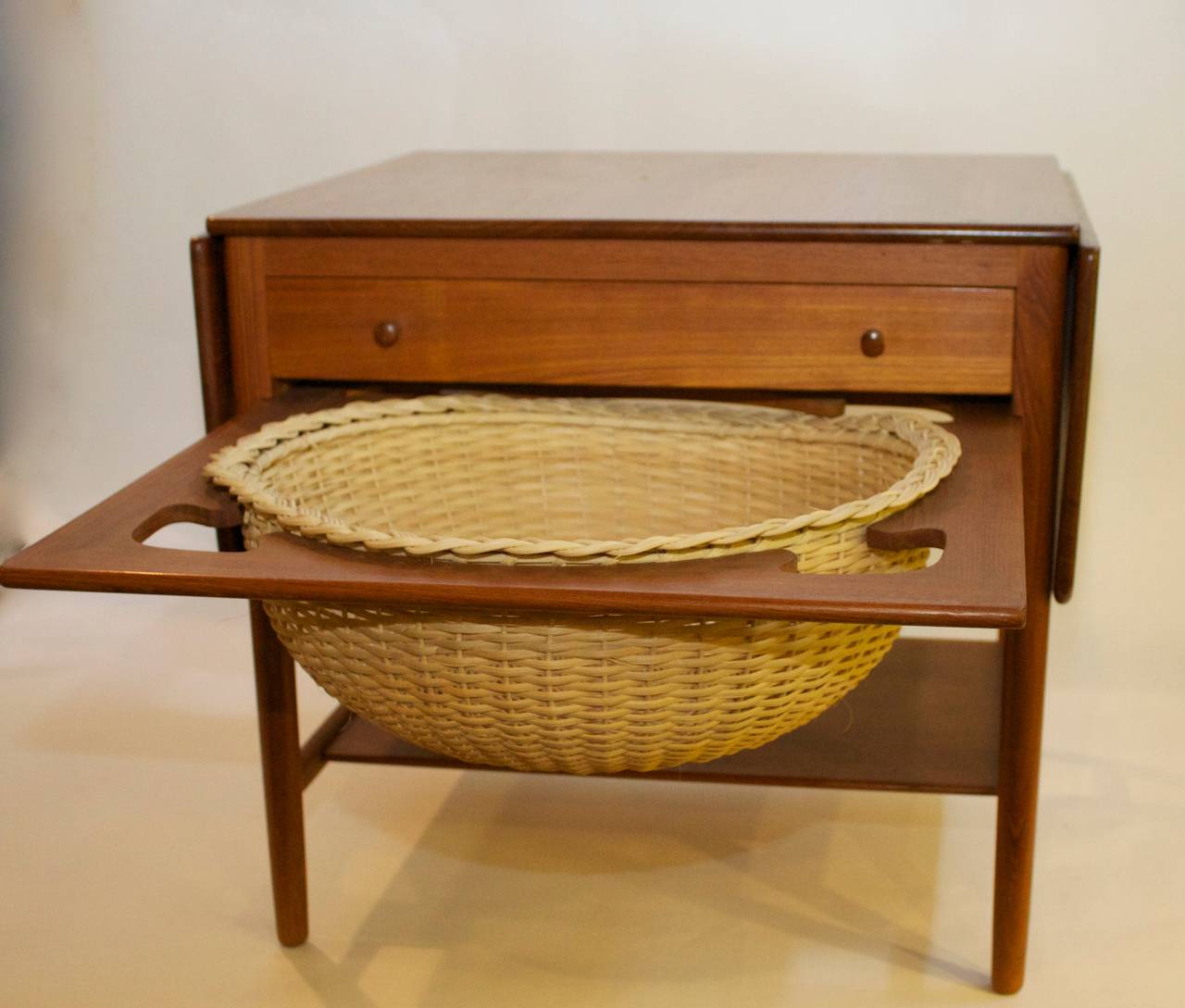 Beautiful drop leaf sewing basket/side table by Hans Wegner for Andreas Tuck.  This table features drop leaves on either side, a drawer with divided storage, a wicker basket/catchall and a lower shelf for additional storage.  A versatile and