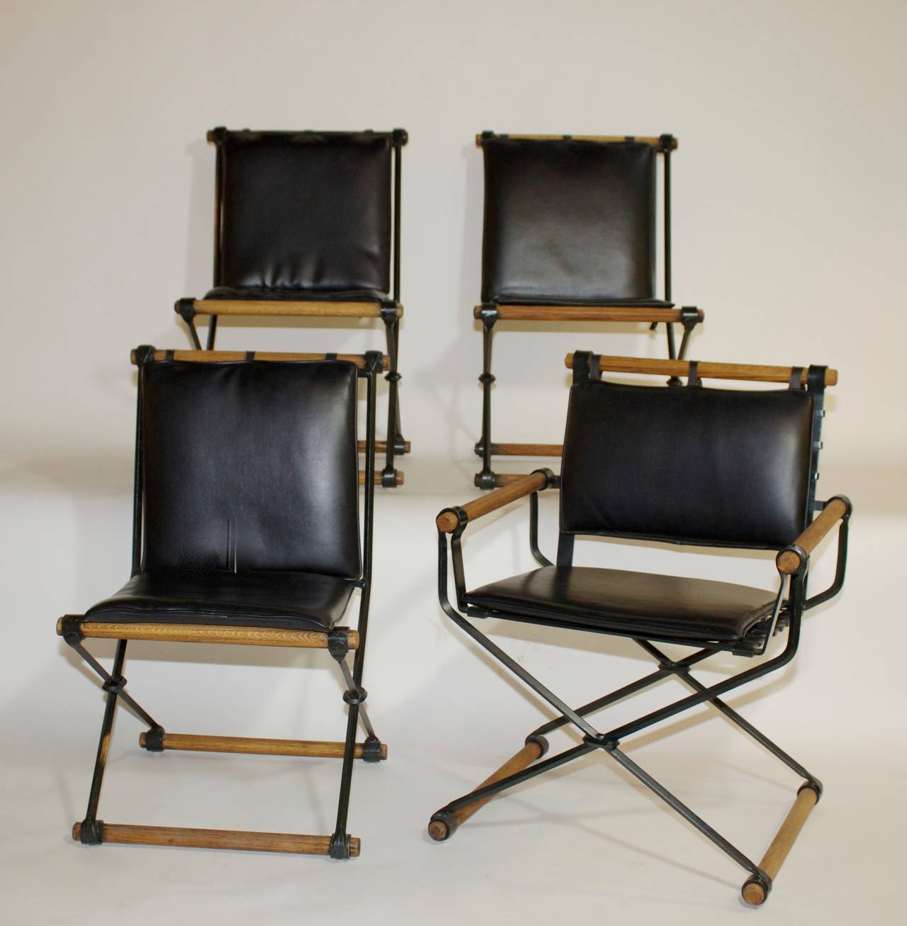 The set consists of one armchair and two side chairs with the original black vinyl upholstered seat/back pads. These are the heavy-gauge wrought iron originals, solid and structurally sound with expected wear and patina to the solid oak dowel