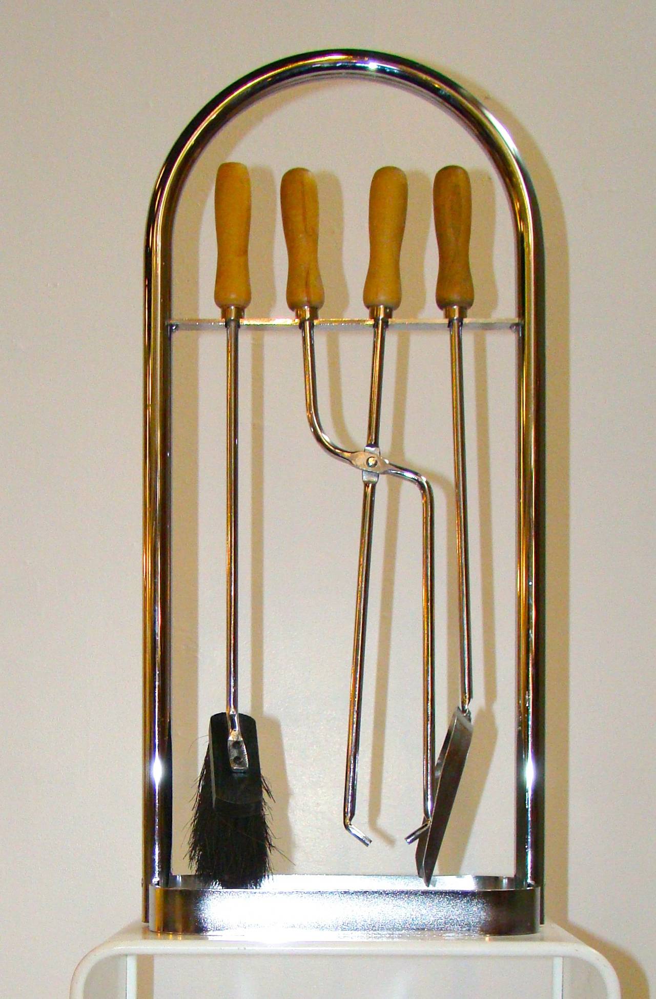Chrome fireplace tools with wood handles housed in an arched chrome tubular  holder.