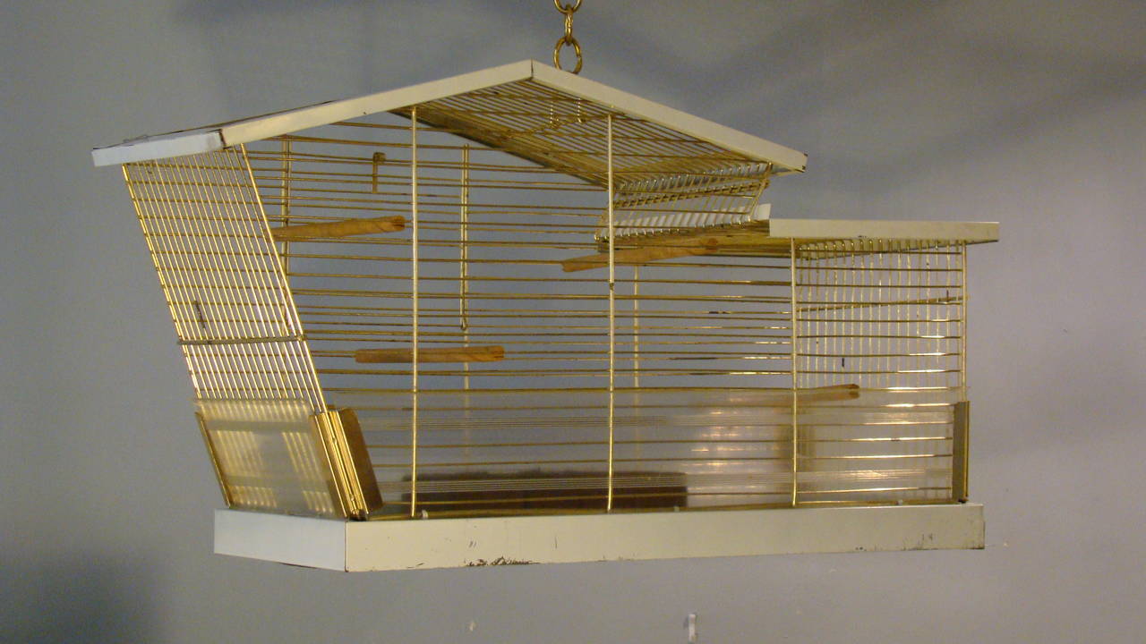 Vintage bird cage in the form of a modern home. Fully functioning bird shelter,
gold tone metal wire with white enamel base and soffit. Use as originally intended for a small aviary shelter or re-purpose to a lamp or terrarium. Unique form.