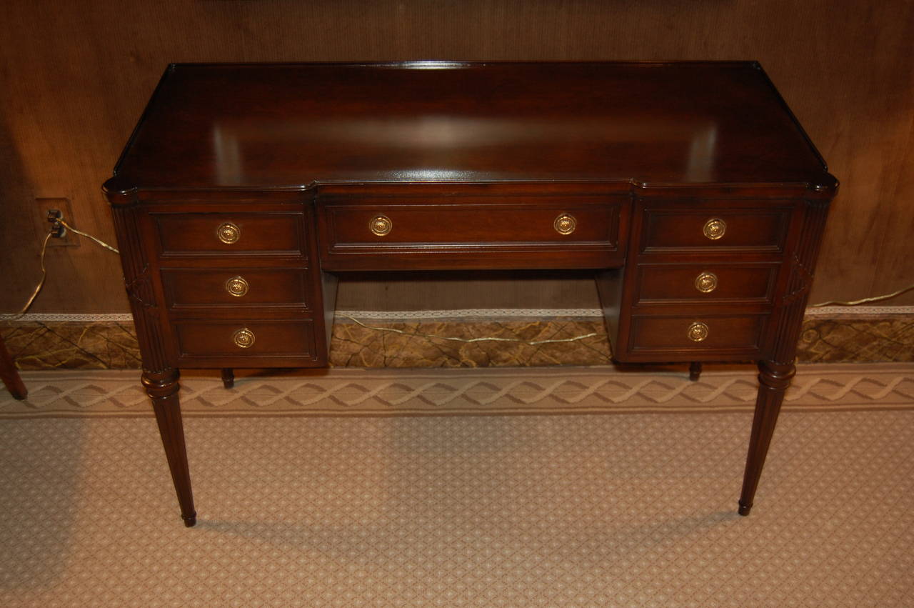 Walnut finished dressing table or desk with tapered, fluted legs and carved columns decorated with carved ribbon ornamentation. The drawers are lined with wallpaper and the center drawer has dividers. The interior of the knee hole is 19 3/4