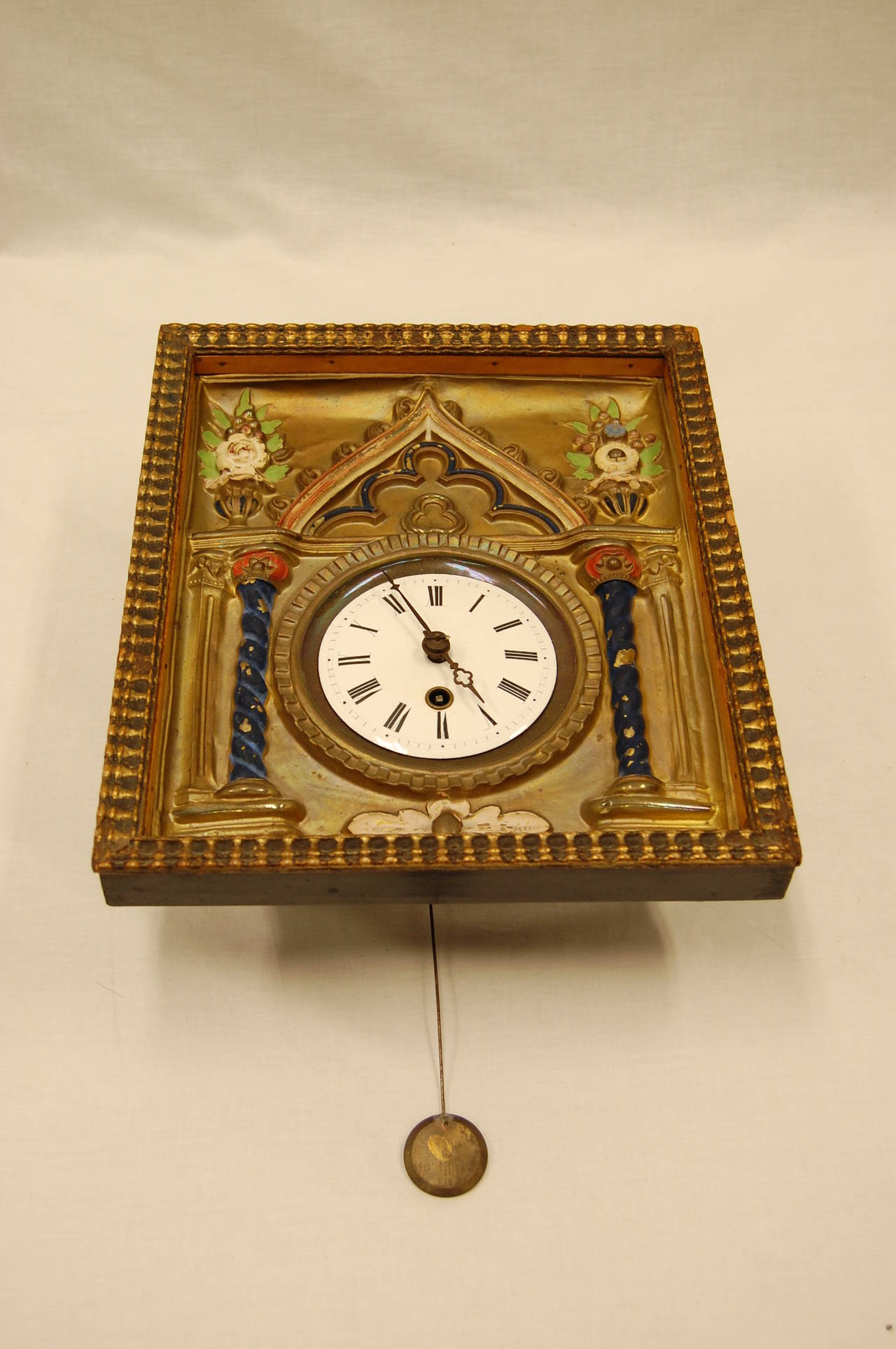 Brass repousse and enamel wag-on-wall clock with enameled dial and roman numerals. While we have owned this clock for many years, we have never really attempted to check to see if it works. The key does wind the mechanism and it will run for a time,
