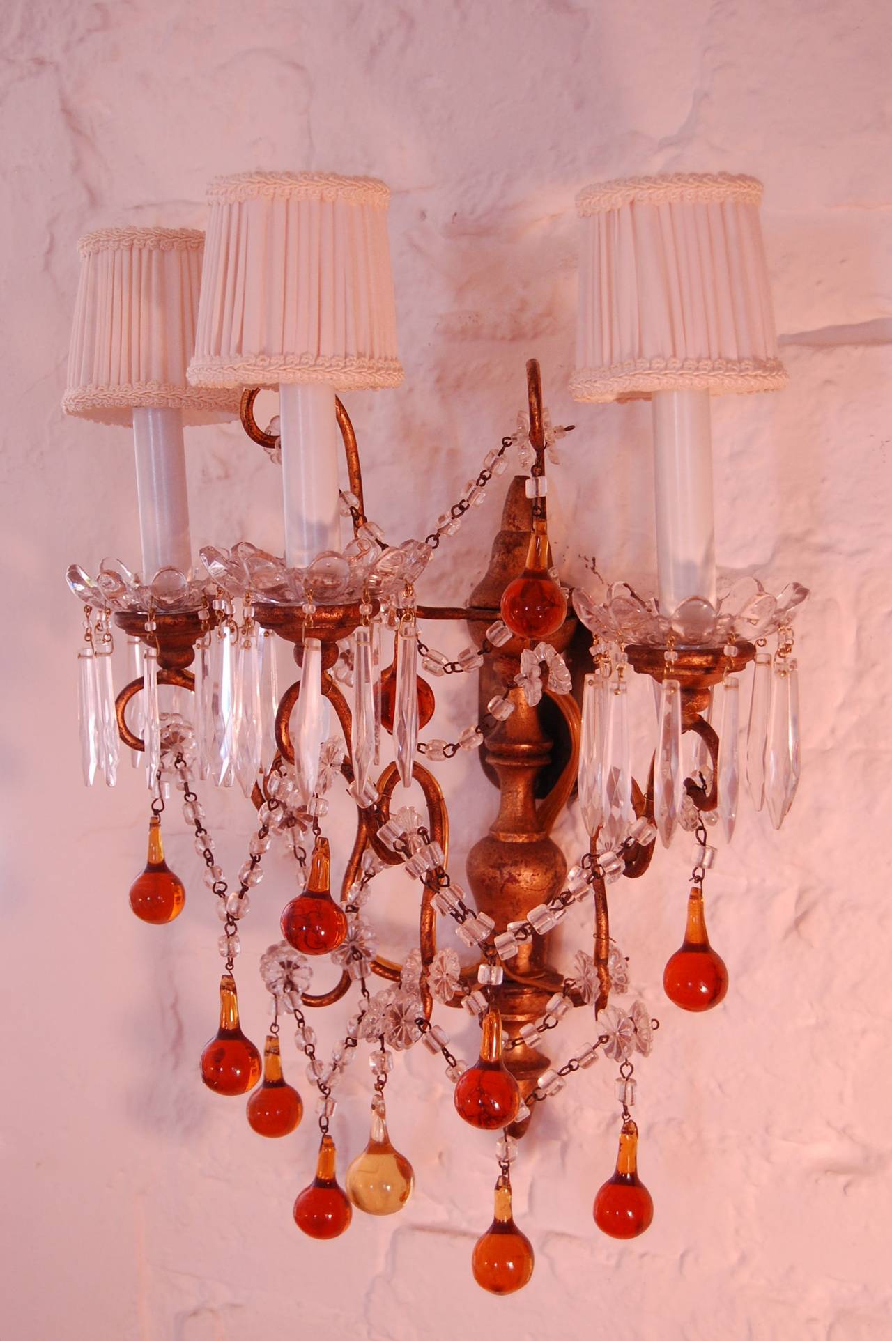 Pair of Italian three light wall sconces with amber glass drops, strands of clear glass beads and glass bobache. The turned wood and gilt back plate has a thin plate to conceal the electrical box in the wall. Possibly early 20th century.