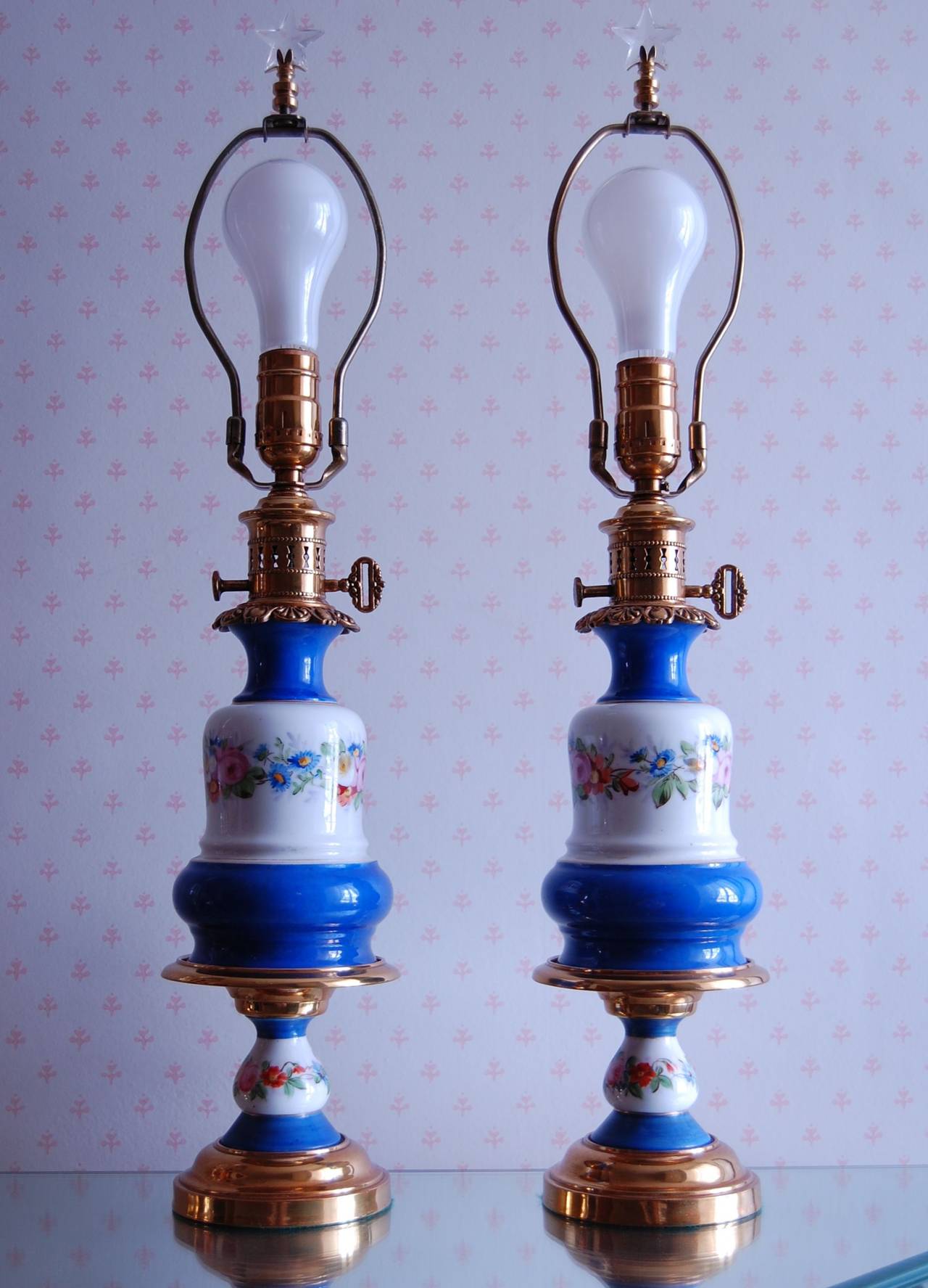 Pair of French oil lamps, circa 1850 with beautiful floral decorations on a white and blue background. It measures 14 inches to the top of the brass burner. Recently rewired with a three way socket, completely cleaned, polished and lacquered.