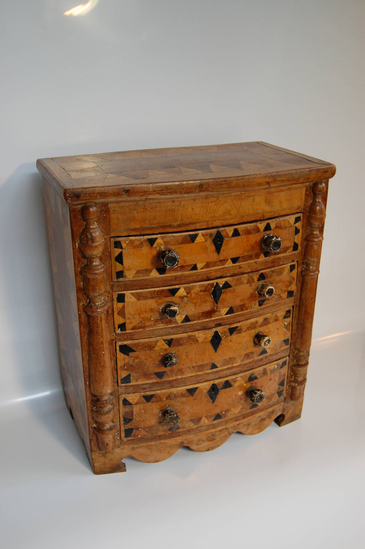 Wonderful American Tramp Art chest of drawers. Solid-end and bow fronted case fitted with four conforming drawers and parquetry inlaid. Three of the original glass knobs have replacement wooden knobs and one glass knob has a section missing. The
