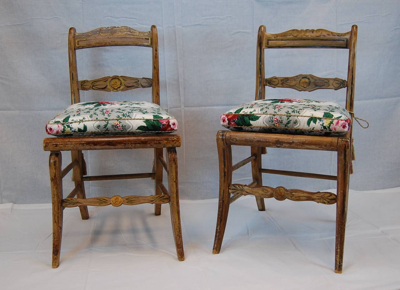 Two similar 19th-century American painted side chairs, possibly from Baltimore, circa 1820-1835. Both have newer seats, one is hand-caned, the other has a rush seat. The pads are cotton floral chintz by Colefax and Fowler printed in England, with