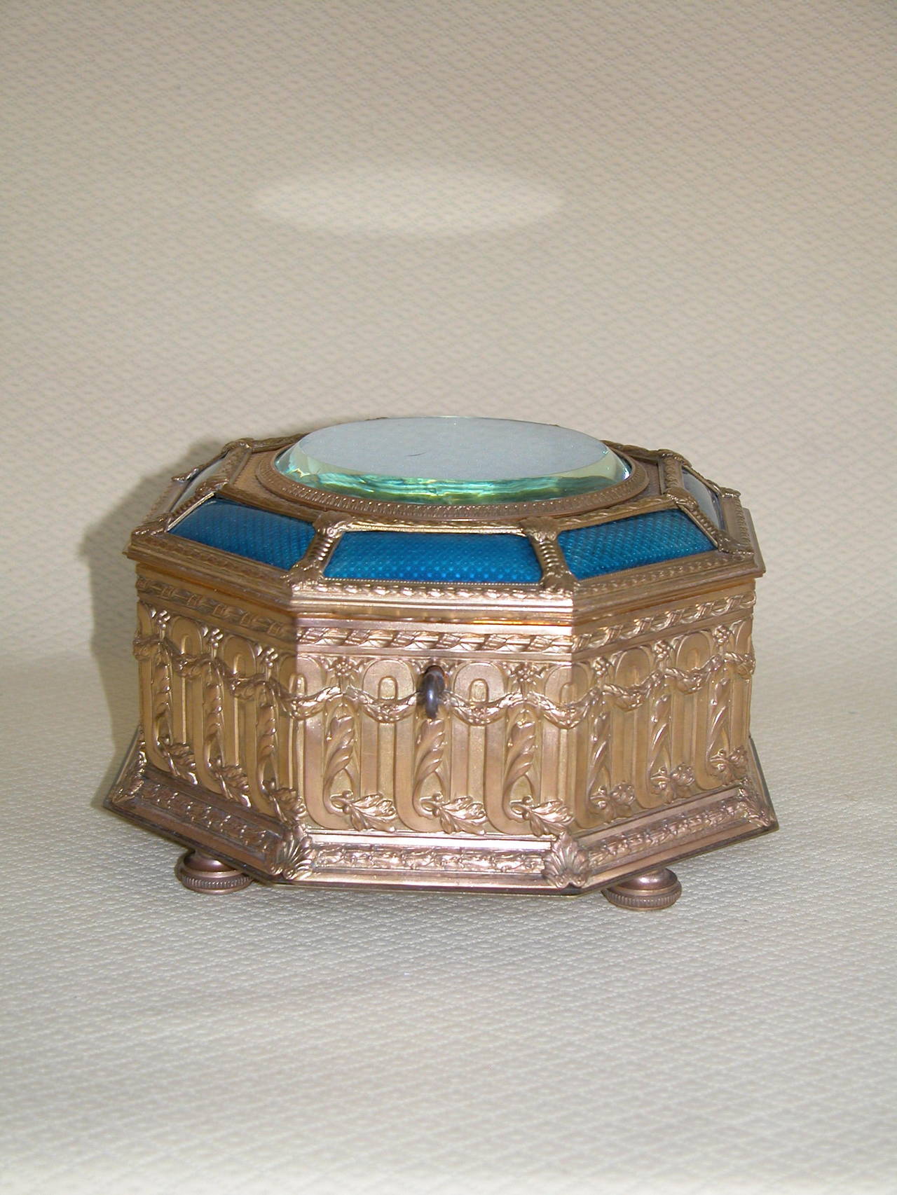 Gold-washed brass box lined with blue silk fabric. Key still works the lock. Clear glass disc in the lid has a minor chip in the top, and the blue enamel is in excellent condition.