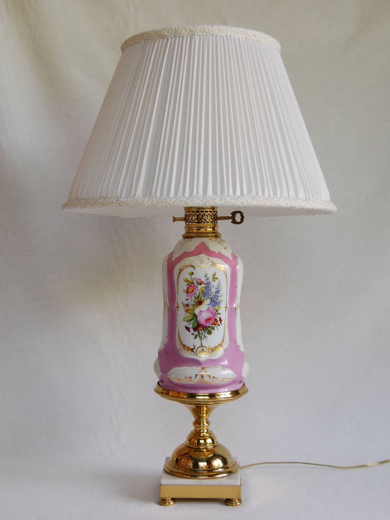 Paris porcelain floral-decorated oil table lamp on a tazza base (possibly not original base). Beautifully decorated in pink and gold with floral bouquets, resting on a polished brass column and marble base. Recently rewired, cleaned, and polished.