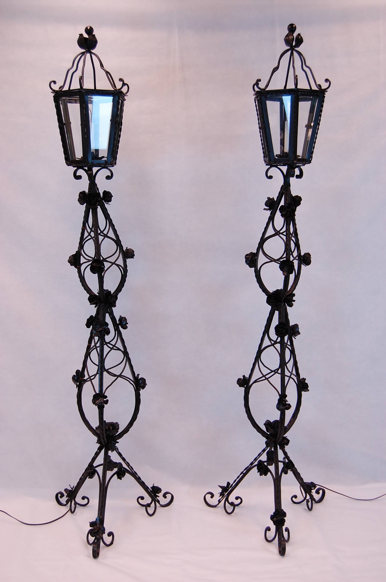 Pair of early-20th-century Italian wrought iron standing lanterns with stamped steel flowers. Professionally cleaned and painted in black lacquer. Wired and in working condition. Uses candelabra size bulbs. Lantern head dimension: 10.5