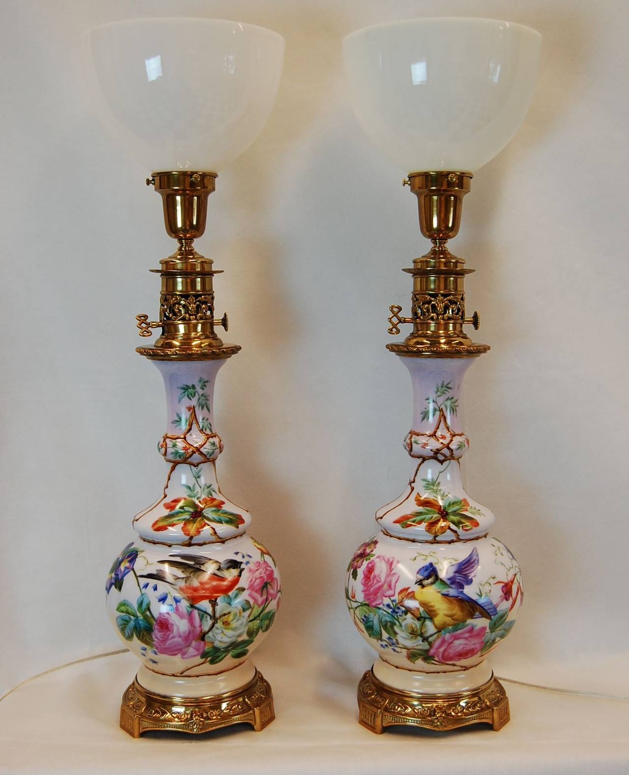 Beautiful pair of hand-painted English porcelain floral and bird decorated oil lamps with original brass bases and fittings, circa 1870-1880. Newly cleaned, polished and rewired with three-way sockets.
