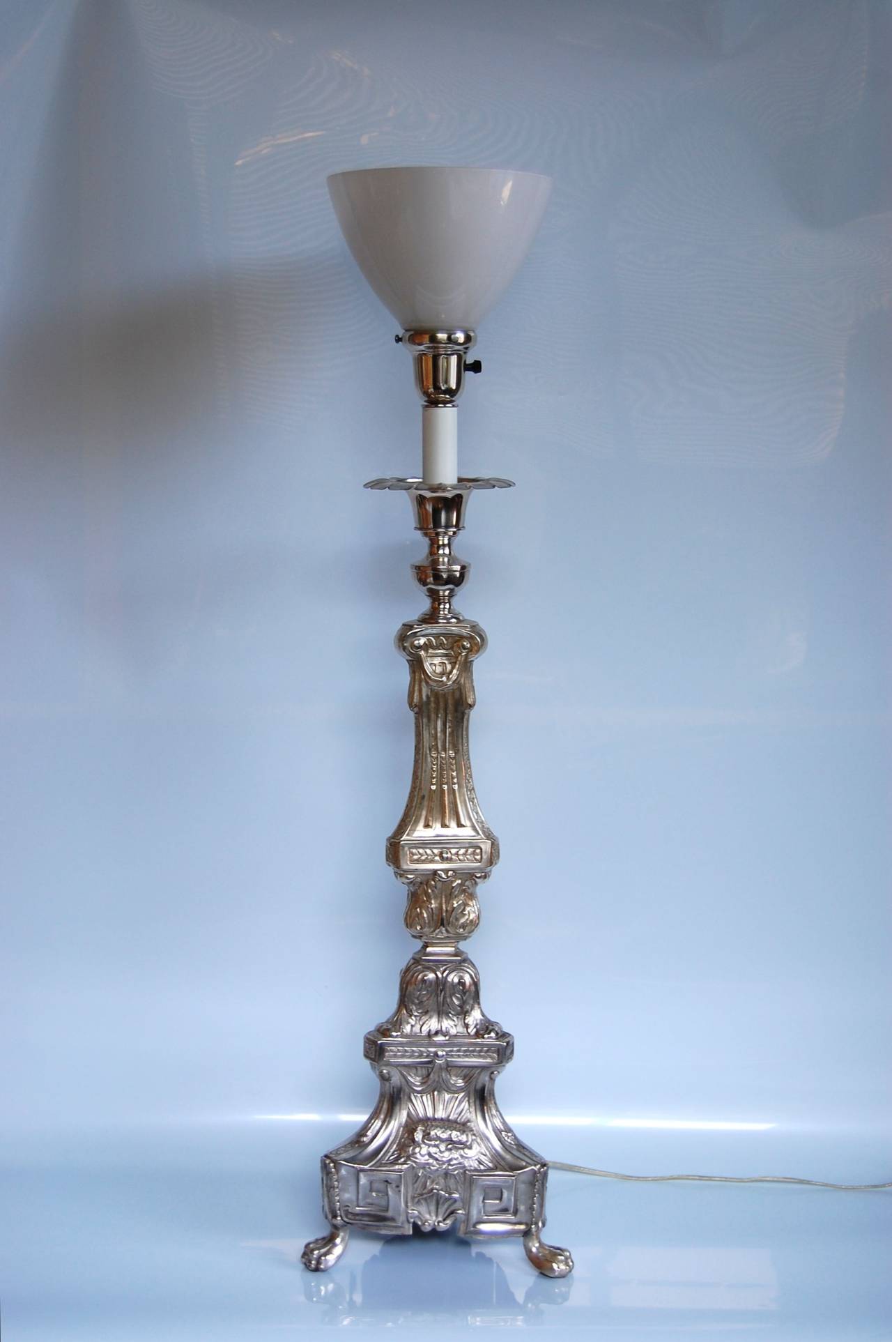 Large silver plate column table lamp that has been lacquered. Decorated with a resting lamb, wheat, grape clusters, and a religious symbol. The lamp was likely made from a mid-19th-century altar candlestick that was not wired until the