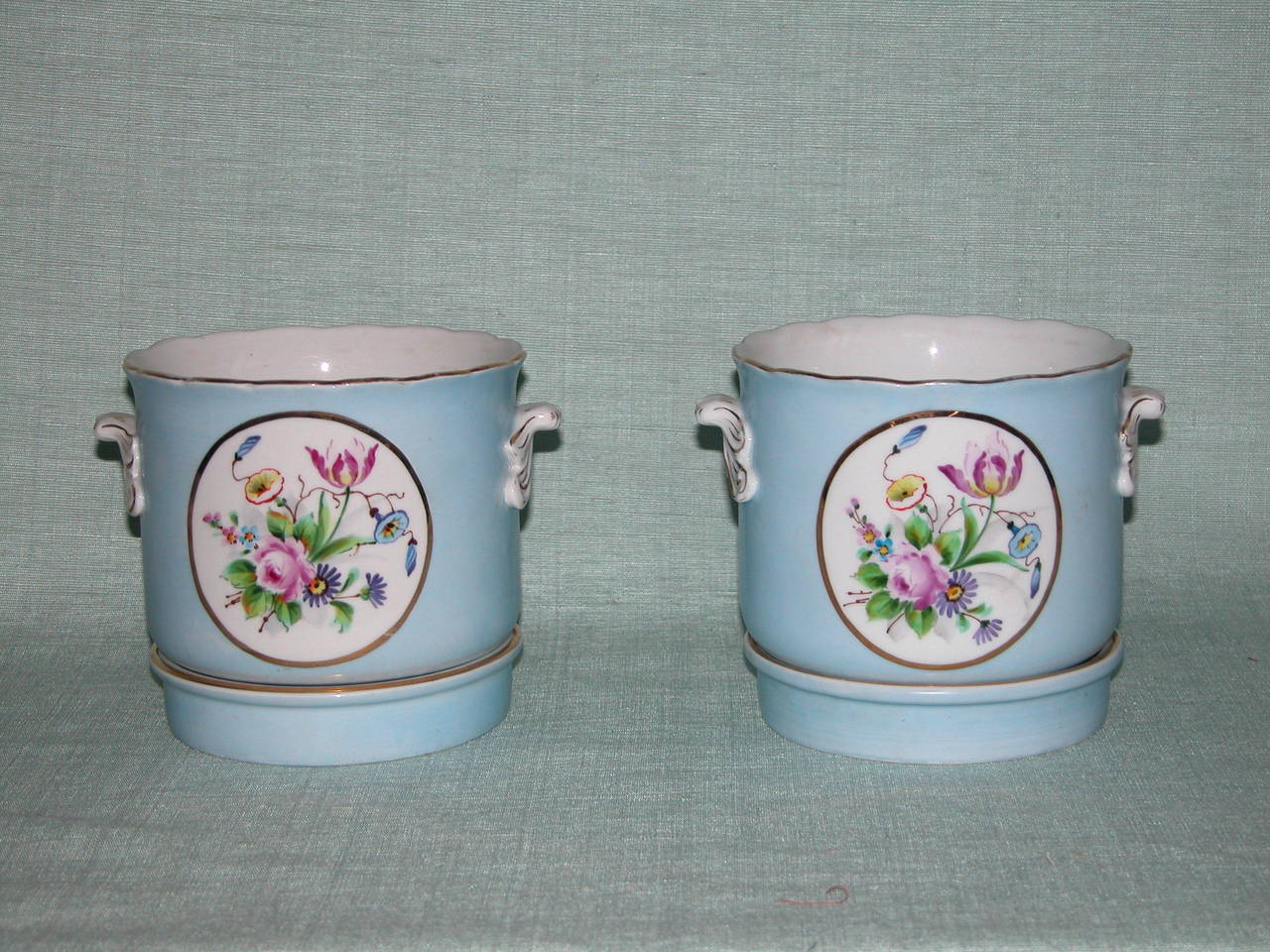 Pair of mint condition porcelain cachepot in a soft periwinkle color, with original saucers. Beautiful hand-painted floral designs on both front and back of pots.