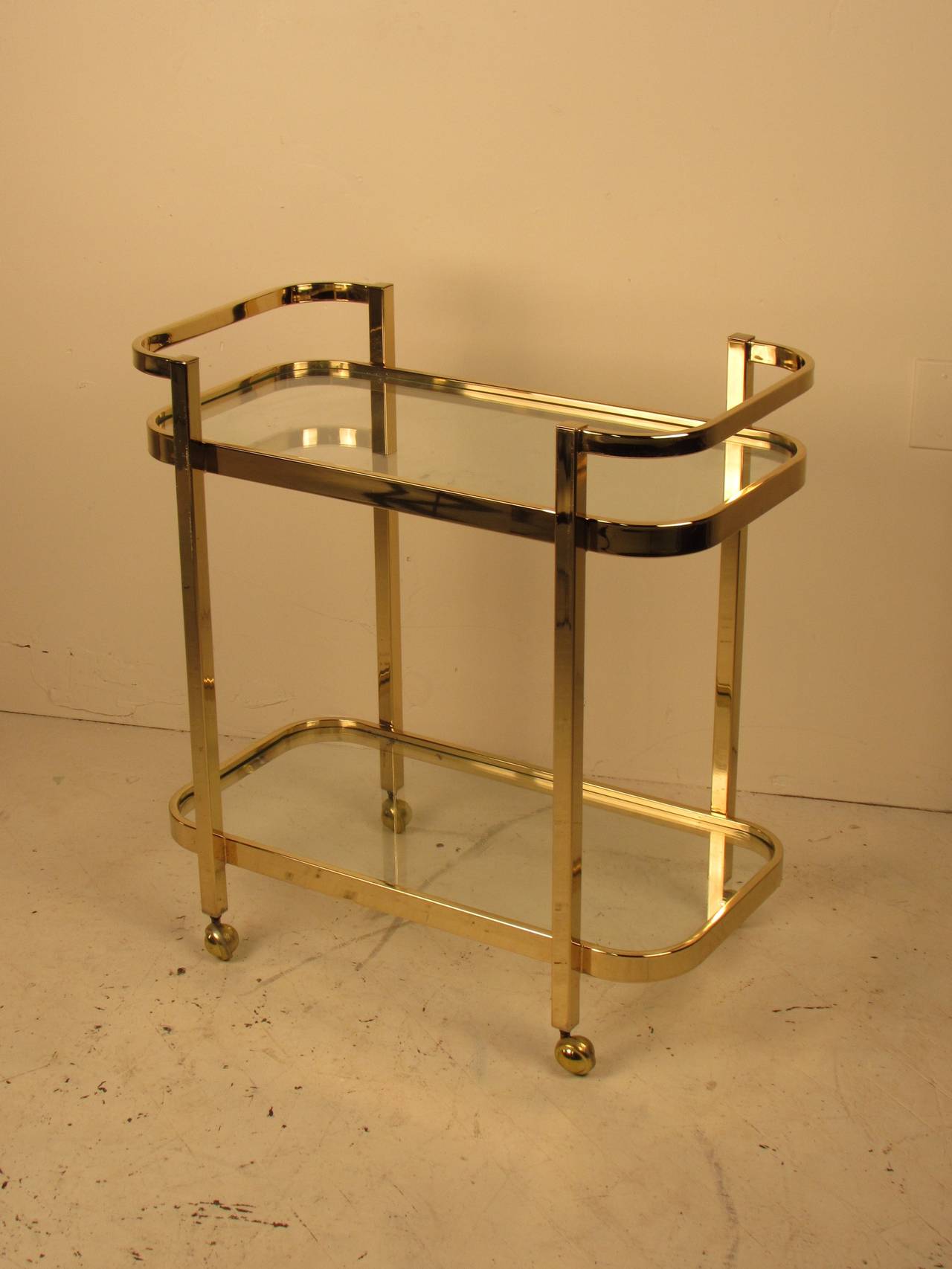 Classic brass and glass bar cart by Milo Baughman for Thayer Coggin. Sleek styling and solid welded construction. Impeccable quality, weight and craftsmanship! 

Brass and glass are both in overall good vintage condition. There are a few worn
