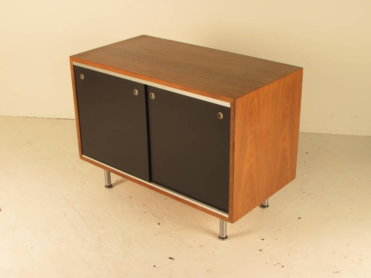 Handsome petite credenza designed by George Nelson for Herman Miller; walnut cabinet with ebonized masonite sliding doors, button pulls and spun aluminum legs. Walnut has just been fully refinished and the entirecabinet shows beautifully.