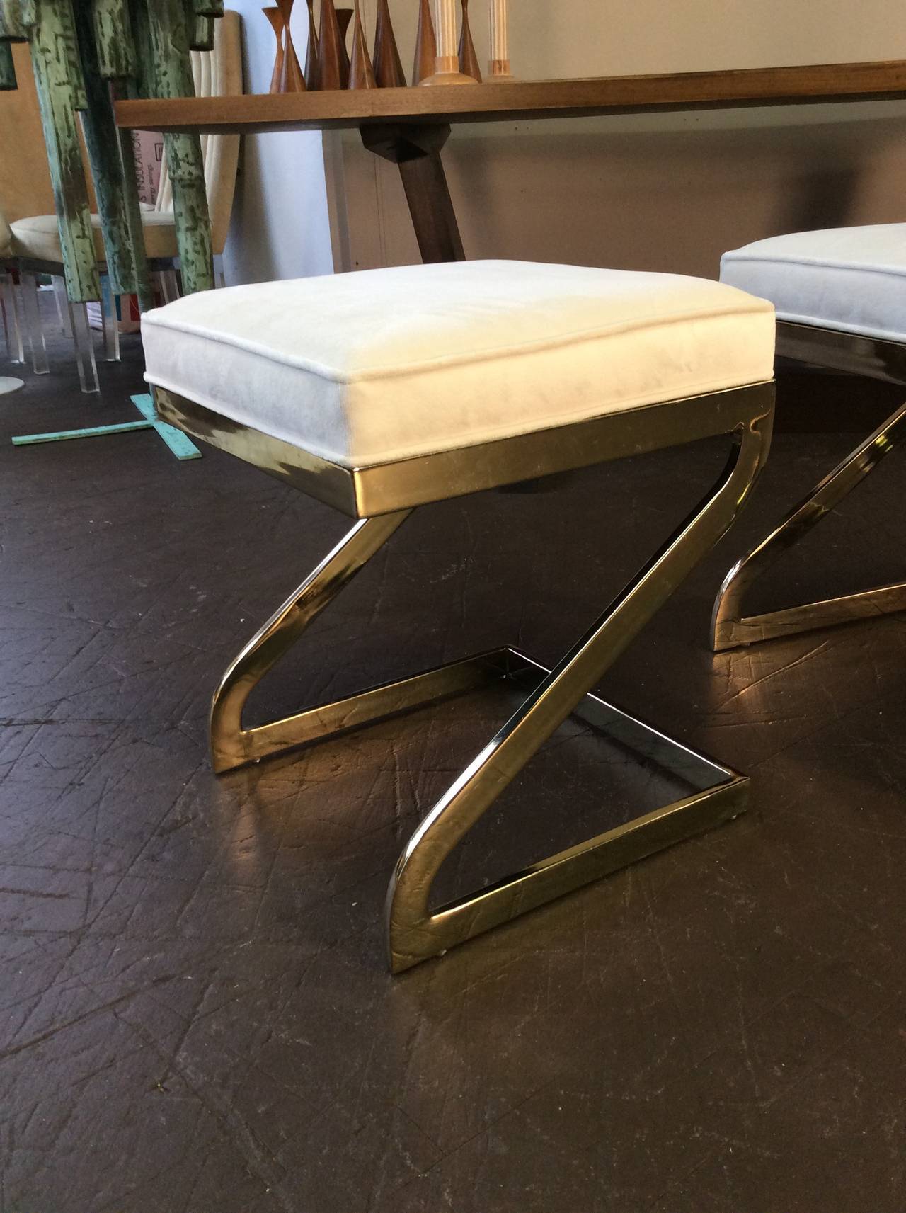 Magnificent trio of cantilevered brass Z-stools, circa 1970. Newly upholstered in white velvet. The brass bases have not been refinished. They do show signs of normal wear. This design is reminiscent of Milo Baughman, Pierre Cardin, Charles Hollis