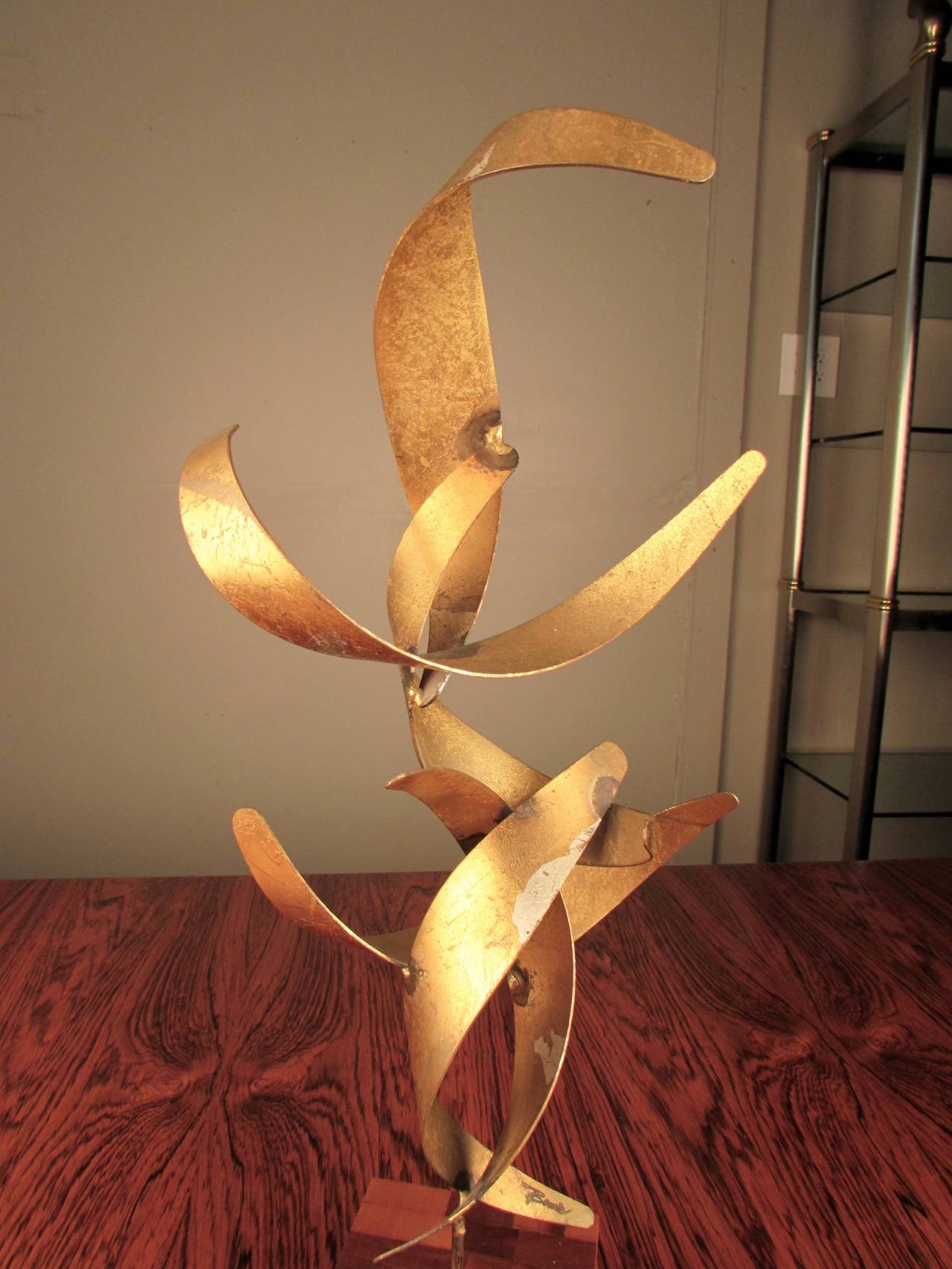 Rare gilded table sculpture signed by William Bowie on staved teak base, circa 1960. This piece is very unusual as most of Bowie's pieces are wall-mounted forms. This delightful gem is a series of rolled steel ribbons welded together to form a flame