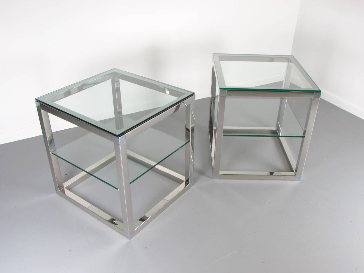 Minimalist chrome cube tables with glass shelves in the style of Milo Baughman, 1970s. These tables are very heavy with solid steel construction. Excellent quality. The chrome is in great condition with minor wear for age. 

We offer free regular