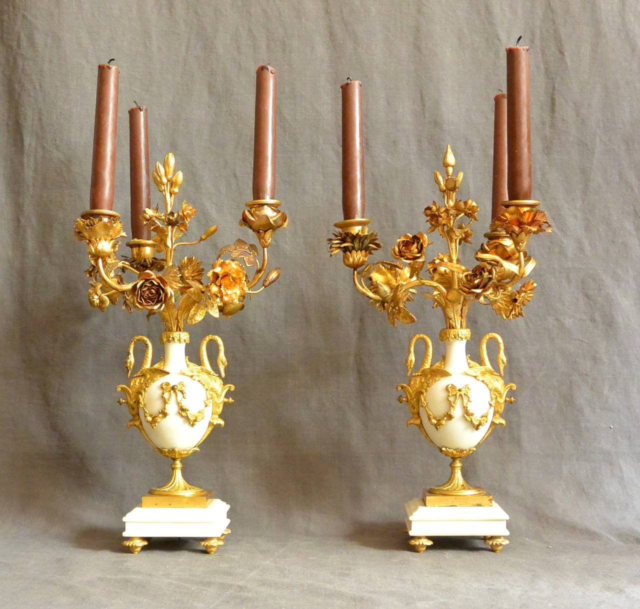Pair of Louis XV style candelabra.  Pair gilt-metal and white marble Louis XV-style three-arm candelabra in the form of swan- handled urns issuing gilt-metal flowers and three-candle sockets on low plinth bases with gilt metal feet.  Continental,