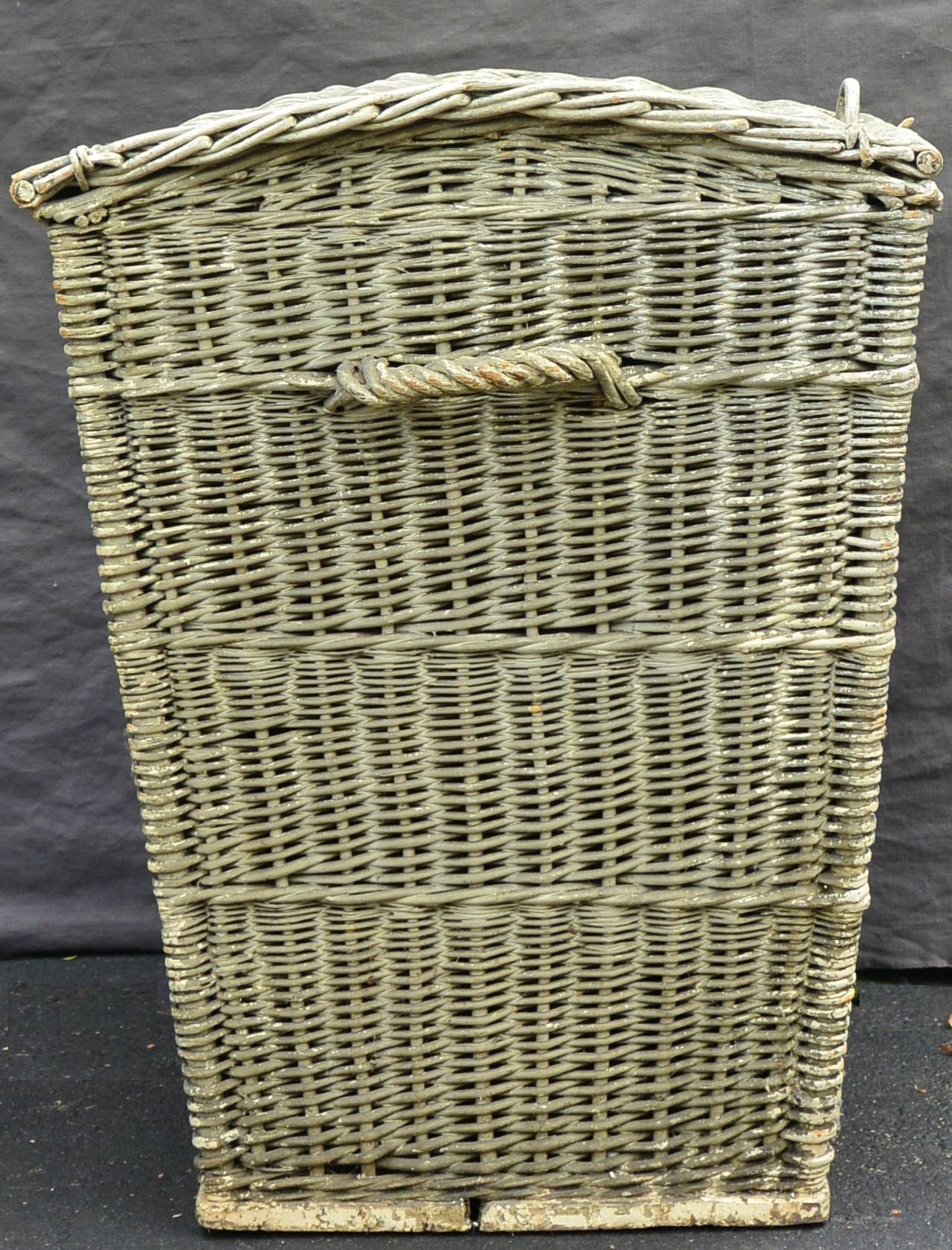 Large American vintage lidded wicker hamper with handles on wood base; painted in pale green milk-wash, and perfect for laundry and hide and seek. 
Dimension: 24