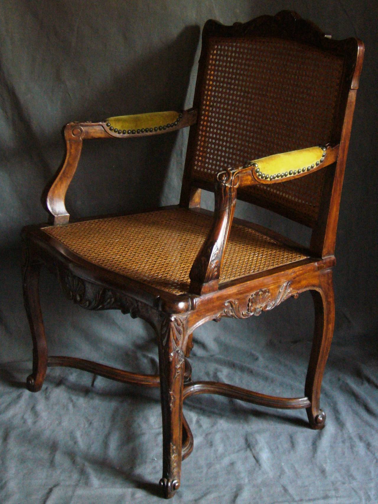 Pair of Louis XV style caned armchairs.  Pair of carved Louis XV style generously proportioned open armchairs, with caned backs, seats and upholstered armrests; with shell-carved back and apron and crossed stretchers. Early twentieth century.
