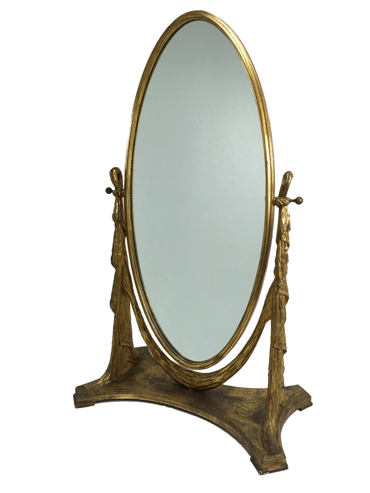 Storybook carved drapery style gilt wood floor mirror at nearly six feet high. Loaded with glamour and movement. Evidence of a break and repair of foot along front of base is barely noticeable.