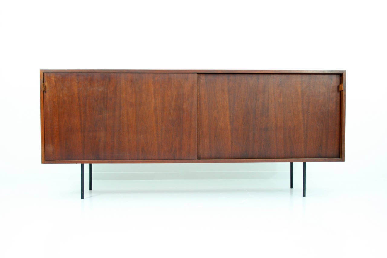 Early Florence Knoll model 116 walnut sideboard / credenza with two sliding doors having leather pulls. Interior lacquered white on inside with oak shelves, Black Iron tubular legs.