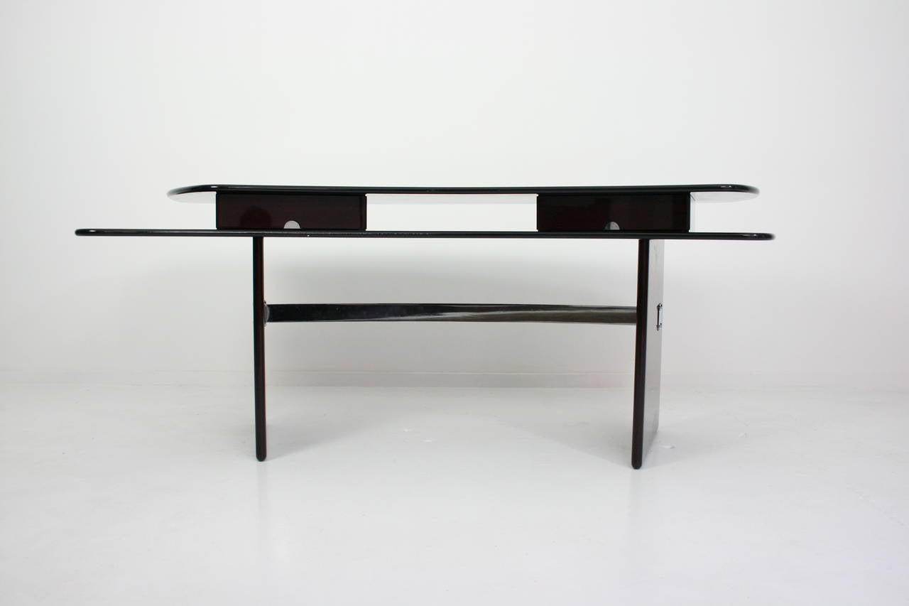 This mahogany desk is a perfect example of the possibilities created by the translation of two finite parallel planes. The two surfaces with their bullnosed high-gloss black lacquer edges resemble dual sabres that come together to create an