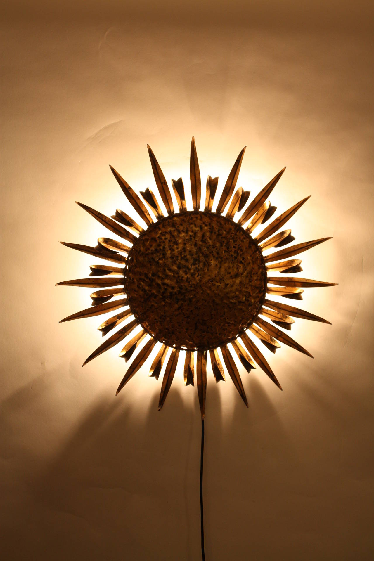 Hand hammered gilt iron sun shaped wall sconce with curved eyelash and straight beams.
Retro illuminated: Three bulbs.

This piece can be placced as a wall sconce or as a flush mount ceiling lamp.
Spain,1950s-1960s