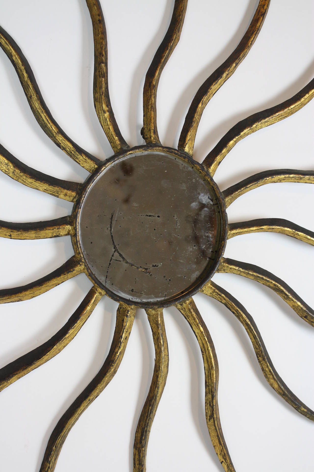 Amazing early 20th century gold leaf iron sunburst mirror with the original patina.

Unusual curved rays creating a sense of movement.

Original mercury glass.