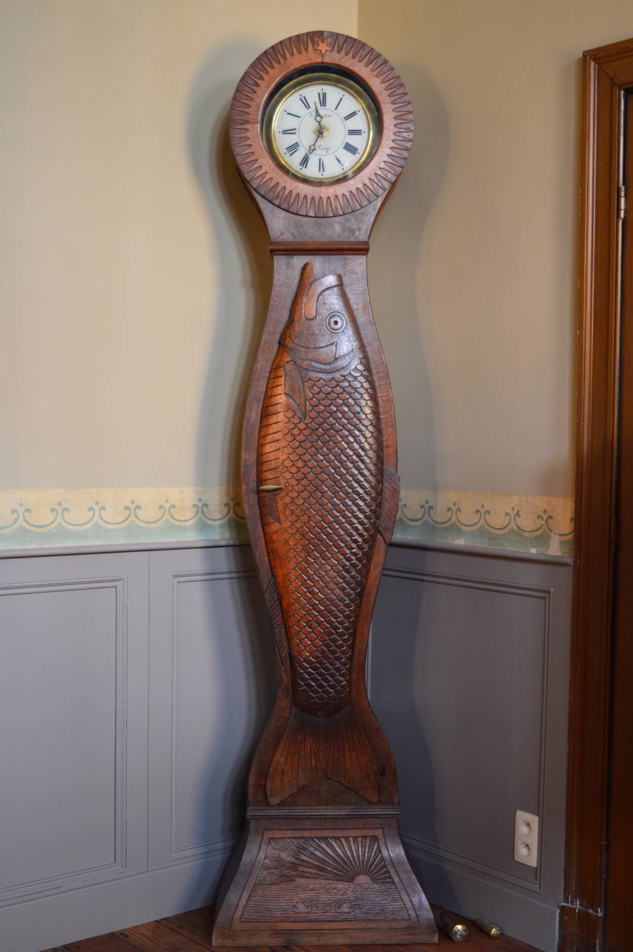This extremely unusual tall case clock was made in the last half of the 19th century in Liege , Belgium. The body is carved oak with a very detailed cast bronze fish handle to open the case door.
The clock face is reverse painted glass (églomise)