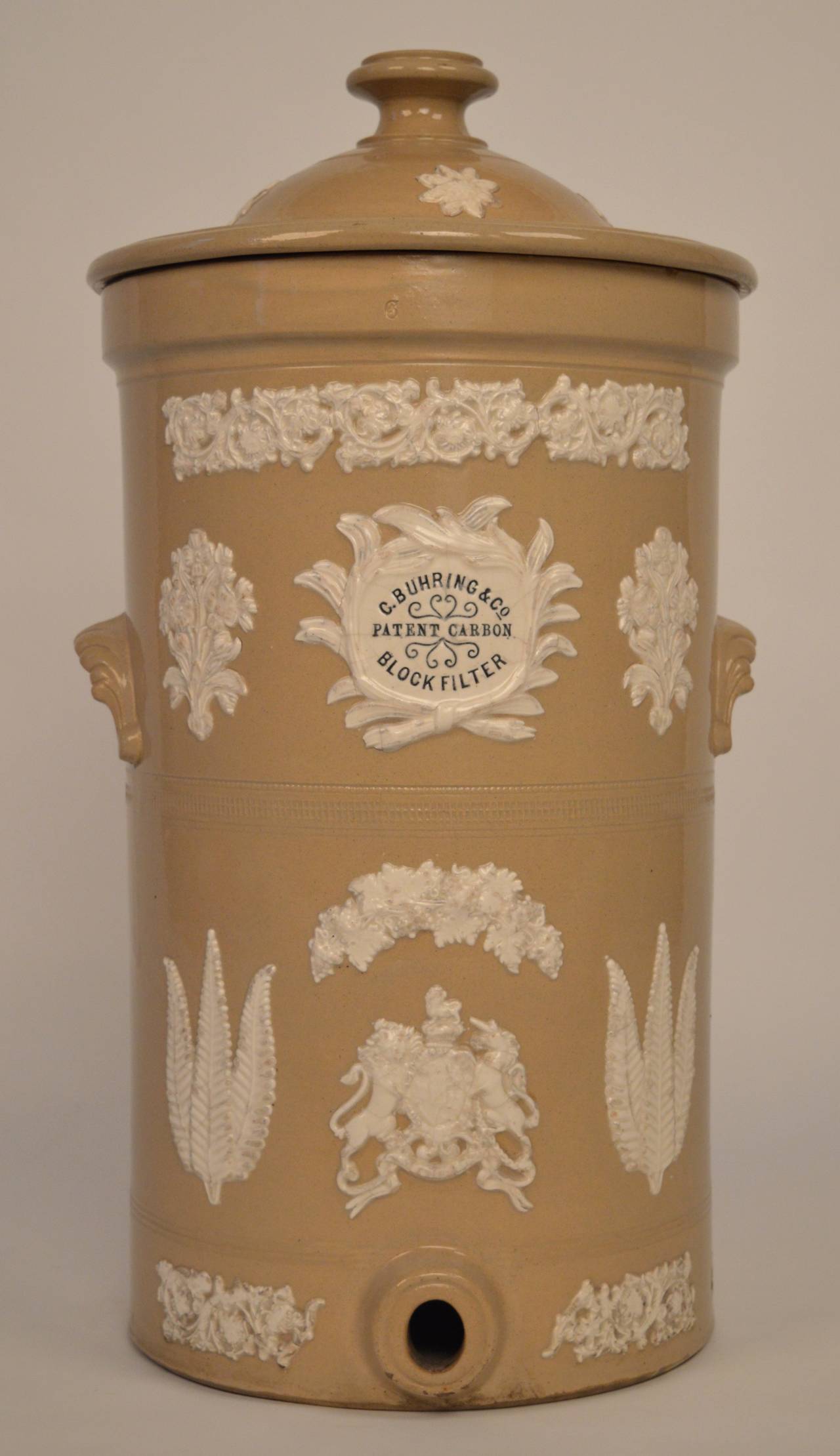 A 19th century English Victorian water sistern made of glazed earthenware with raised foliate decoration .
The center shield is inscribed:
