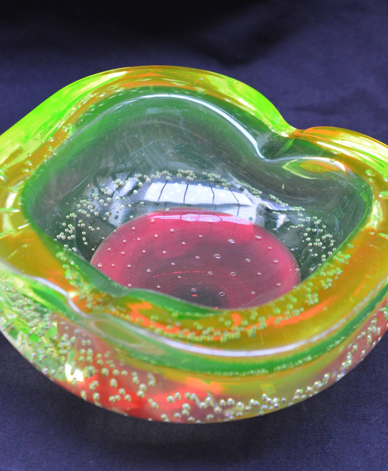 This 1960's Murano glass bowl has a blood red glass center encapsulated in uranium glass. Uranium glass is no longer produced because of the radiation raw uranium produces. 
Uranium has a very special light capturing quality that makes the glass