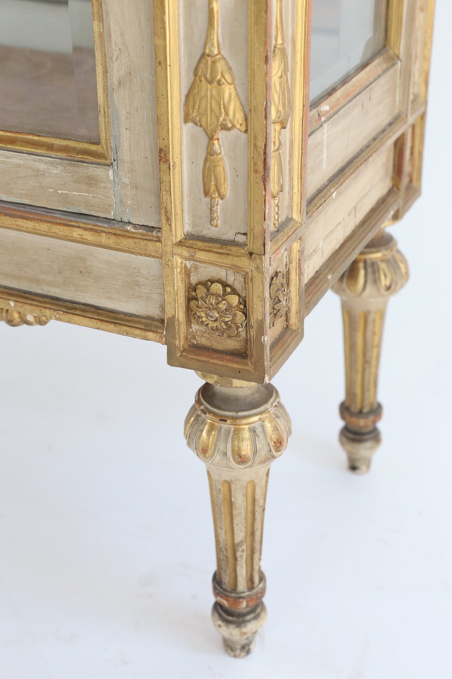 19th century antique neoclassical cream painted and gold leaf vitrine.

The cornice is centered by an open carved ribbon over a pair of doors
fitted with beveled glass panels flanked by stiles carved
with pendant bellflowers and headed with leafy