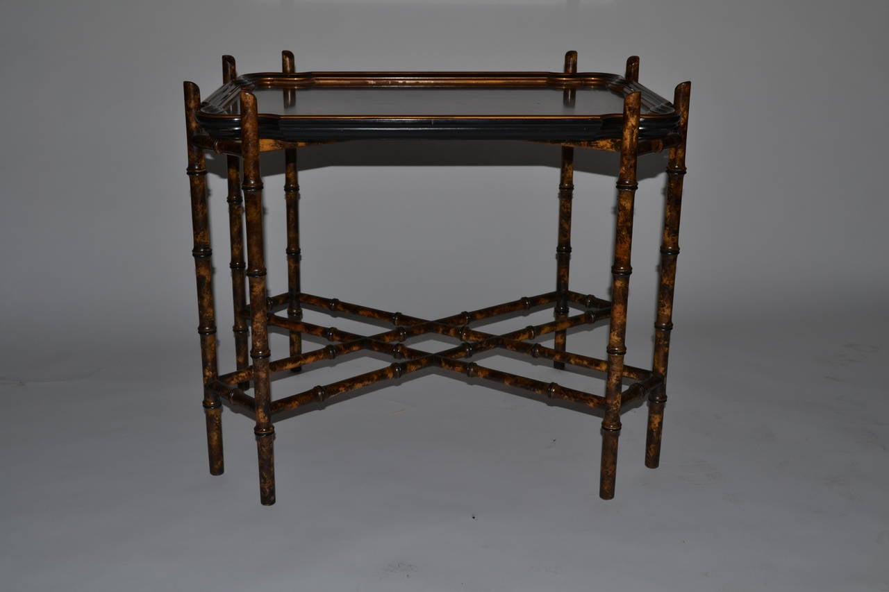 Baker tea table with faux bamboo base and black painted wooden shaped top with bevelled sides.

Perimeter of top painted with two gold pencil stripes.  Interior band features lattice with flowers in corners.