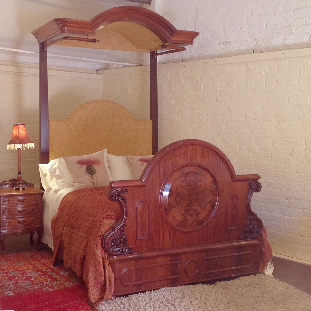 A magnificent Victorian mahogany half tester bedstead with shaped foot panel and tall canopy. The foot panel has burr veneer panels and fine carving. The tall shaped corniced canopy has rail for side drapes and back curtain. We have re-upholstered