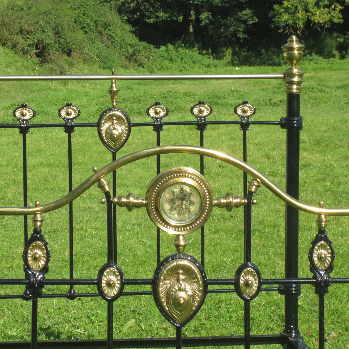 A fine brass and iron bedstead from the late Victorian era with ornate brass decoration. The central brass plaque on both the head and foot depicts a peacock. The foot of the bed has a serpentine brass top rail, under which sits a brass ring with