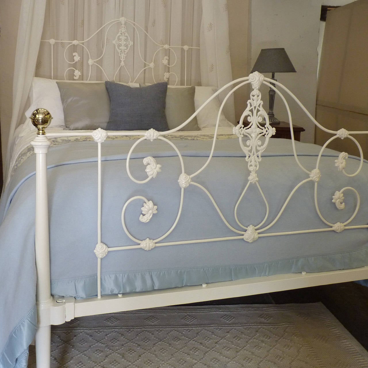 A fine example of a cast iron half tester bed finished in white. The ornate iron work on the panel decoration is typical of the era, as are the four tapered posts. The tall back posts support a half round canopy, from which drapes can be