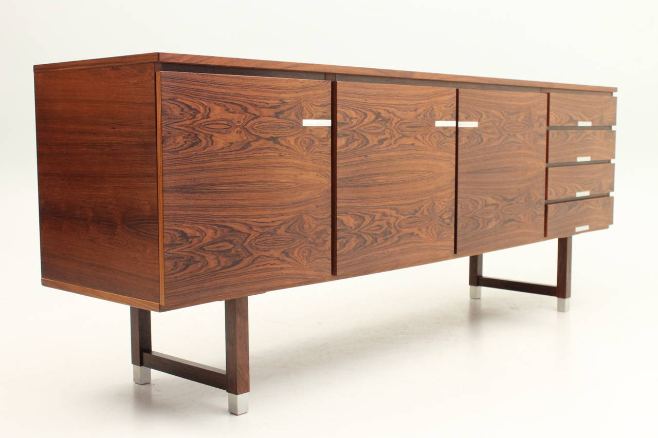 Incredible rosewood credenza by Kai Kristiansen for PSA Møbler. This storage piece features three large adjustable shelf areas as well as four small drawers. The dark Brazilian rosewood grain perfectly compliments the aluminum opening accents. This