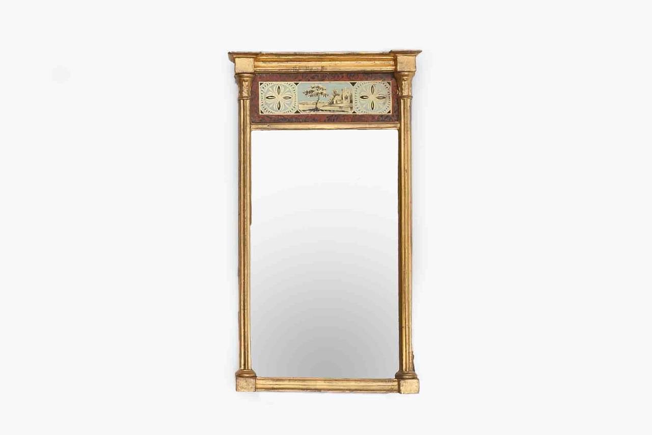 Early 19th Century American wall mirror with original glass. Reeded rounded columns and corinthian capitals make the side supports. Above the mirror glass is a glass panel that is hand painted, verre eglomise showing a pastoral scene with church and