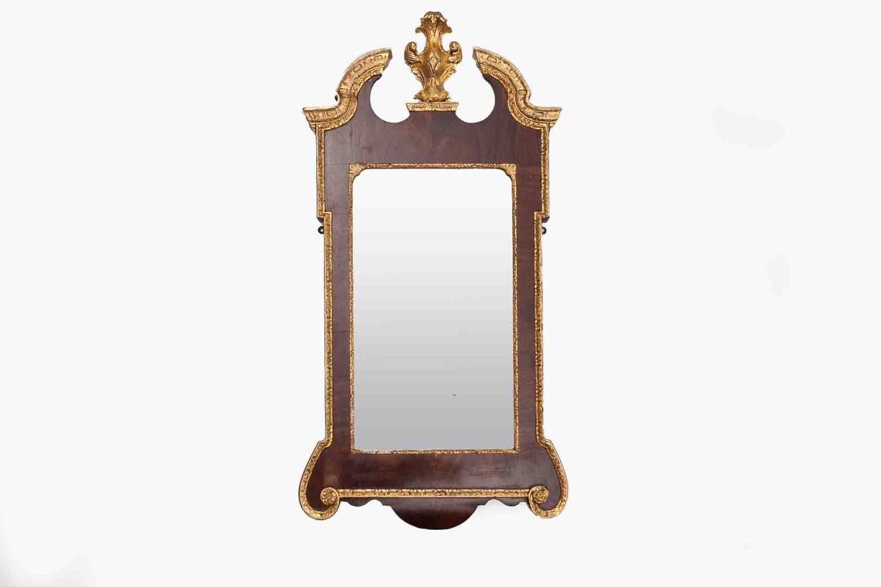18th Century George II walnut and parcel-gilt mirror. The rectangular and bevelled plate within an eared rectangular frame. Surmounted by a moulded cornice with swan's neck cresting centred by a leaf-wrapped cartouche, the lower edge with shaped