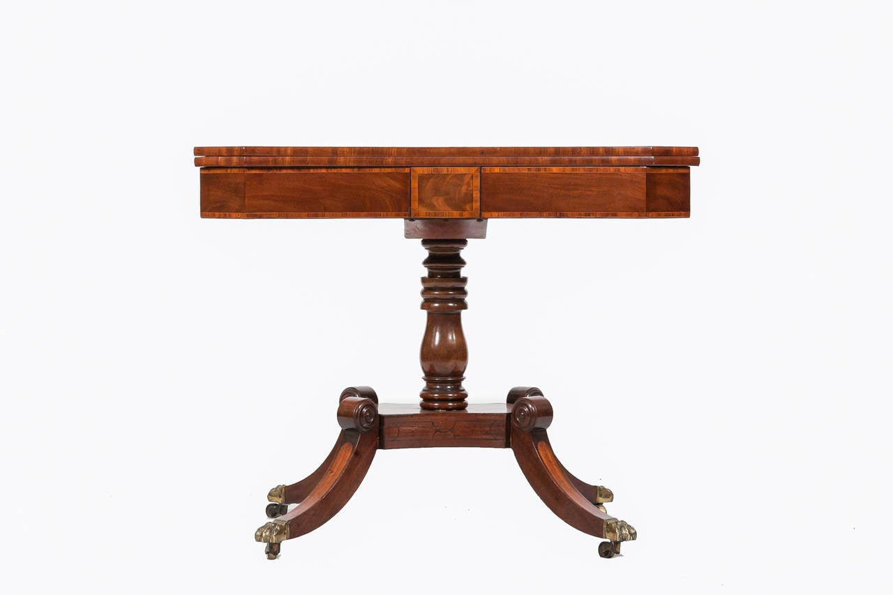 Early 19th Century William IV mahogany pedestal card table, it has four down-swept legs which terminate on original brass casters. The top is cross-banded and swivels to reveal an interior compartment with all original features.