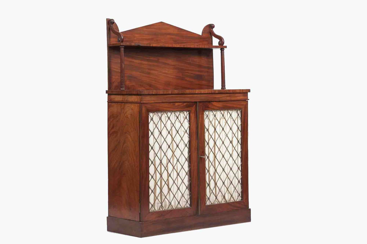 19th Century Regency mahogany chiffonier. The galleried top with turned supports above a pair of brass grille lined doors, opening to reveal a shelved interior flanked by a pair of columns raised on a platforms base.