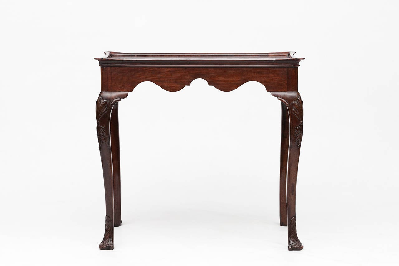 18th Century George II Irish mahogany silver table. The rectangular top with raised moulded dish top edge above scalloped frieze supported on cabriole leg terminating on carved trifid foot.
