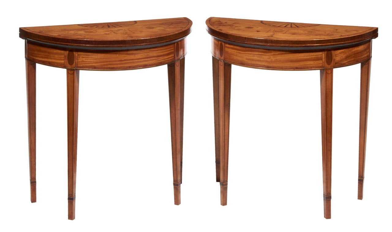 Early 19th Century George III pair of satinwood demilune card tables. The top inlaid with a fan, classical urn and trailing foliate, above square tapering ebony inlaid legs.
