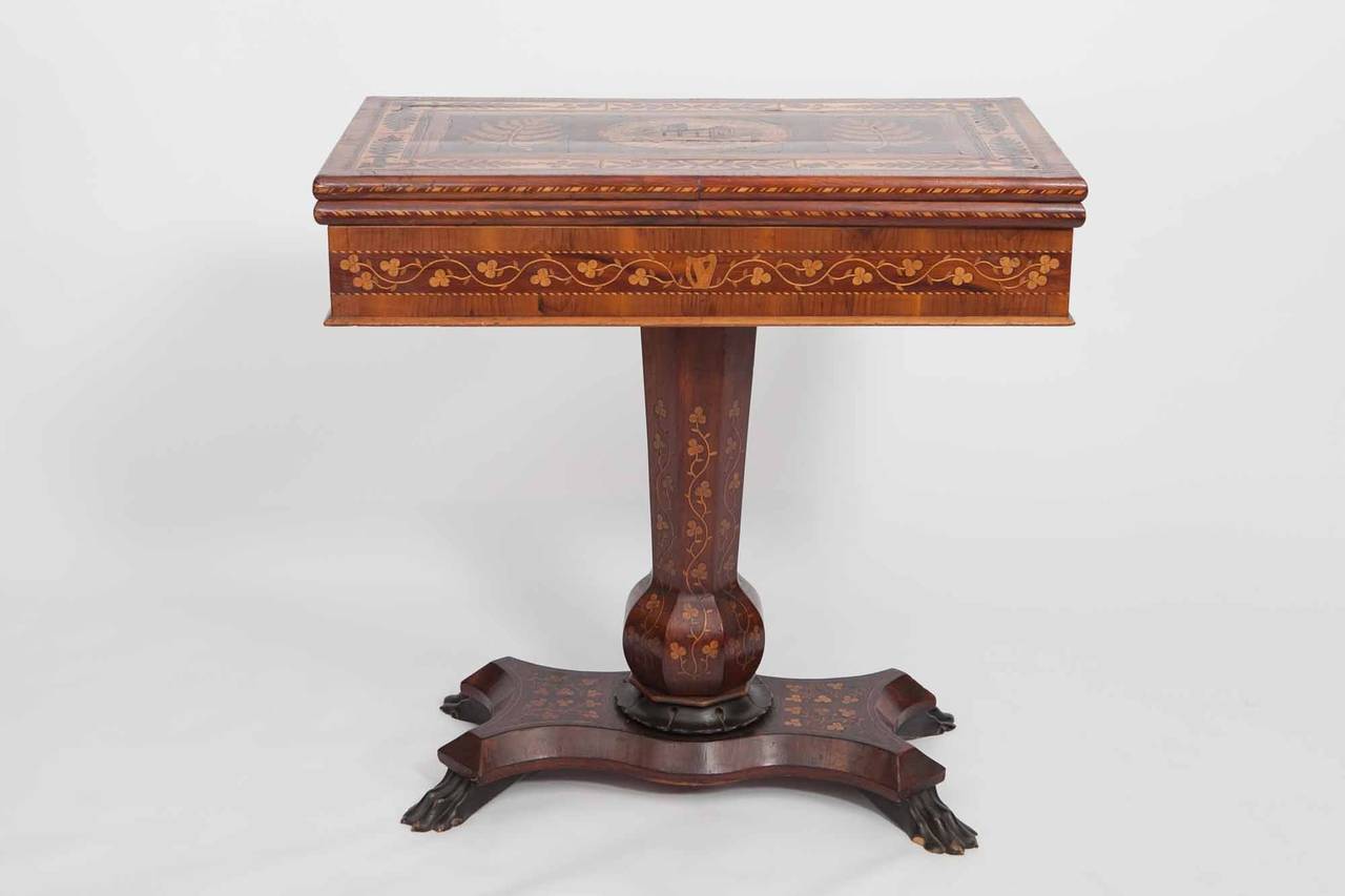 Irish 19th Century Killarney-ware games table. A rectangular fold-over top with central inlaid scene depicting Muckross Abbey, with backgammon and chess boards, above a baluster stem over in-curved quadripartite base.