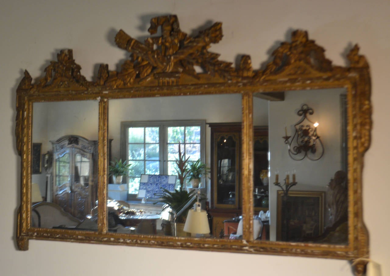 Wood carved and gilded mirror with sectioned cannelures and beaded carving with top attributes of wheat and a torch with ribbon, flanked by detailed floral motifs. Some gilding is missing and there are two minor cracks/repairs (see photos).
